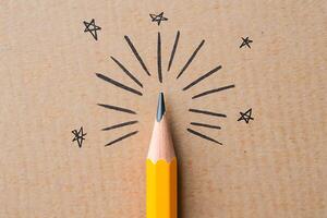 A yellow pencil point with lines and star symbols demonstrating creativity and education concept on a wooden surface photo