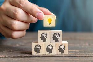 Person building a team of minds with a bright idea represented by a light bulb over wooden cubes for conceptual thinking photo