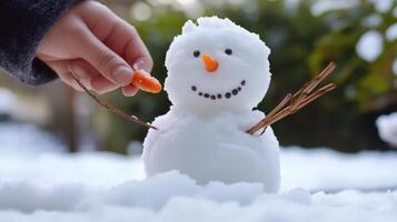 Child's hand adding a carrot nose to a small snowman. photo