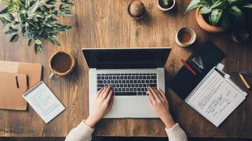 Overhead view of hands typing on laptop at a wooden table. photo
