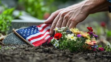 A hand places flowers and a flag on a grave photo