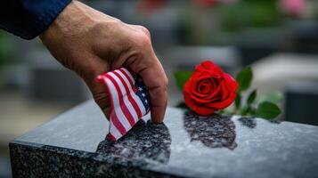 A hand places a small flag on a memorial stone photo