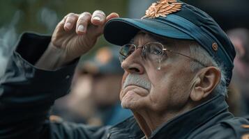An elderly man with a tear wearing a military hat salutes photo