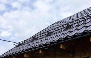 Closeup snow guard for safety in winter on house roof top covered with ceramic shingles. Tiled covering of building. Snow guards on the roof photo