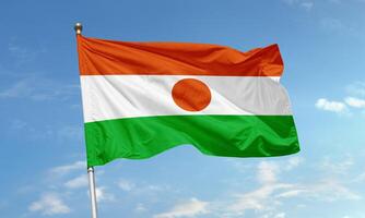 Flag of Niger waving against blue sky background photo