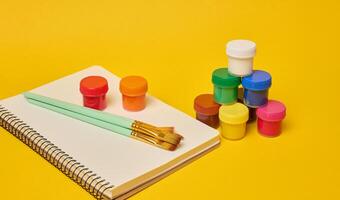 White spiral notebook, brushes and colorful paint cans symbolizing art photo
