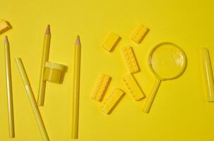 Collection of yellow stationery, building brick, and magnifying glass on a yellow background. Pencil, marker, jar included. Creative or learning concept. photo