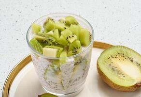 Chia seed pudding topped with diced kiwi sits on a plate with halved kiwis and a spoon. photo