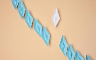 A line of blue origami paper boats with one white and the outline of the missing one, symbolizing uniqueness or a missing element photo
