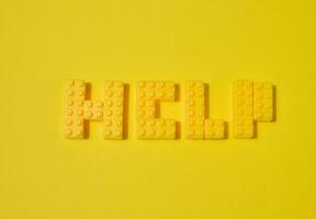 The word HELP, made from yellow toy blocks, is placed on a yellow background photo