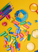 Vibrant collection of colorful school supplies, building bricks, letters, and learning items scattered on a yellow background. Play and education concept. photo