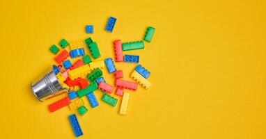 Vibrant colorful building bricks spilling from a silver metal bucket onto a yellow background. photo