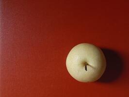Drama A Refreshment from the Top of a Pear. A fresh pear is seen from above sitting on a very fine grained red table with dramatic minimalist lighting and shadows. photo