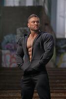 Muscular man posing confidently in urban setting during daylight showing strength and fitness photo