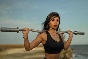 Strong woman lifting weights by the water during sunset for fitness and empowerment photo