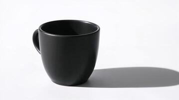 Close up photograph of a matte black coffee cup on a white background. Strong shadows define the cups form, focusing on texture and detail in a minimalist still life style. photo
