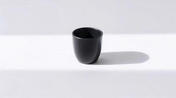 A photograph of a minimalist still life a matte black coffee cup on a clean white background. Strong shadows define the cup's form. The composition is simple and elegant. photo