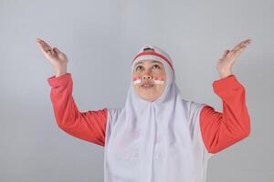 Muslim woman with Indonesian face paint raising hands and looking upward with hopeful expression in emotional Independence Day celebration symbolizing pride and gratitude photo