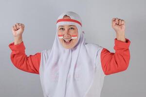 Indonesian woman in hijab with flag face paint celebrating with fists raised and smiling photo