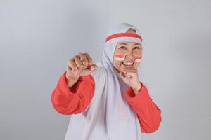 Energetic Indonesian woman in red and white hijab smiling brightly with fists raised in playful boxing pose and flag-painted cheeks during spirited Independence Day celebration photo