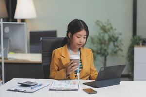 A woman in a business suit sitting at a desk with a laptop and coffee photo