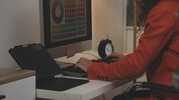 A woman in an orange jacket is typing on a computer video