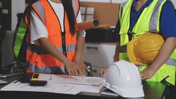 Two construction workers standing at a table with a blueprint video