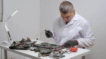 Technician Repairing Computer Circuit Boards, Technician in a white lab coat soldering and testing computer motherboards. video