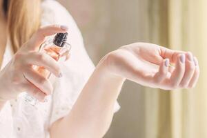Beautiful young woman holding a bottle of perfume and applying it on her wrist photo