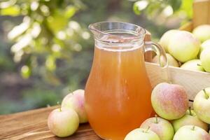 Apples, box of apples and pitcher of fresh apple juice on wooden table photo