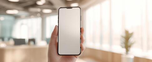 The smartphone held in a hand against a bright office background. photo