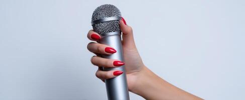 The hand holding a microphone with striking red nails in a minimalist setting. photo