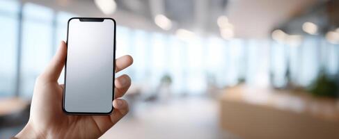 The smartphone held in hand against a bright modern office background. photo