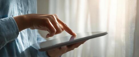 The person interacting with a tablet by a sunlit window. photo