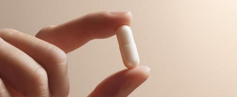 The hand gently holds a white capsule in soft light settings. photo