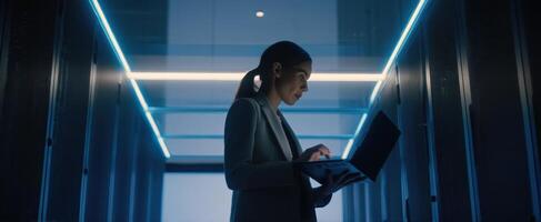 The woman working on a laptop in a modern server room environment. photo