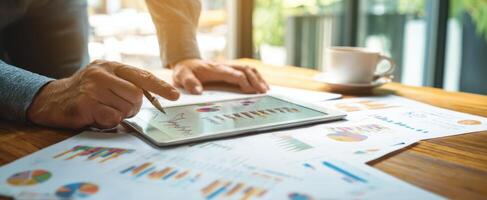 The professional analyzing data on a tablet with paper reports on a wooden desk. photo