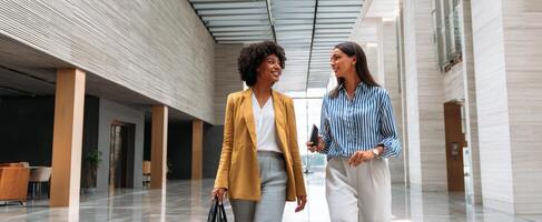 The two confident women walking and chatting in a modern office hallway. photo