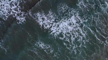 Aerial view of the ocean's dynamic waves with white frothy crests against deep blue and green hues, showcasing the sea's natural rhythm and vibrant beauty from above, evoking tranquility video