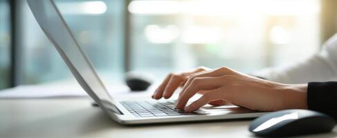 The hands typing on a laptop in a modern workspace setting. photo