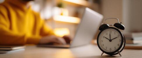 The vintage alarm clock beside a focused person working on a laptop. photo