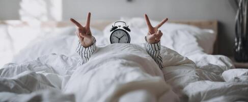 The playful person wearing an alarm clock celebrating happiness in bed. photo