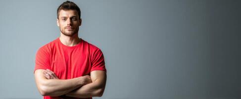 The confident man standing with arms crossed wearing a red shirt in studio setting. photo