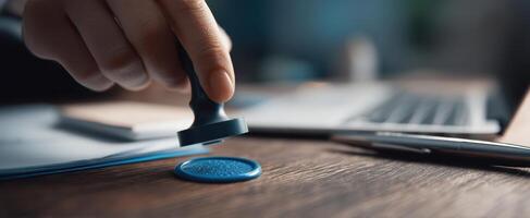 The hand applying a blue stamp on official paperwork at a desk. photo