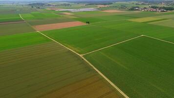 Aerial view of Bavarian farmland in Germany during summer. Green fields, dirt roads, and small chapel at crossroads. Solar panels in the background highlight sustainable farming and renewable energy. video