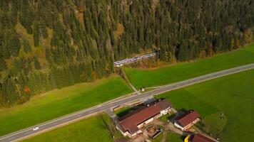 Drone shot of a regional train nearing Bayrischzell station during fall, framed by colorful autumn trees in Bavaria, Germany. A serene view of nature and railways in perfect harmony video