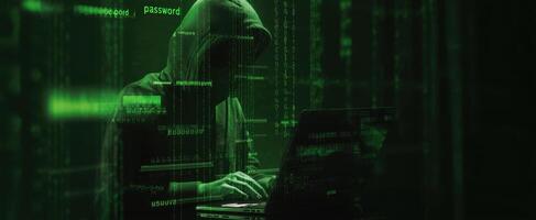 The hacker working intently on a laptop in a dark, green-lit environment. photo