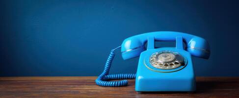 The blue rotary phone resting on a wooden table against a deep wall. photo