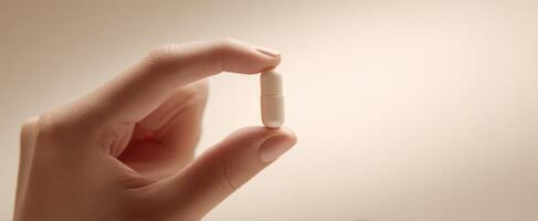 The hand holding a white capsule against a soft, neutral background. photo