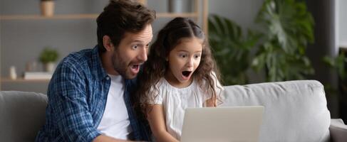The father and daughter experiencing joy and surprise together while using a laptop. photo